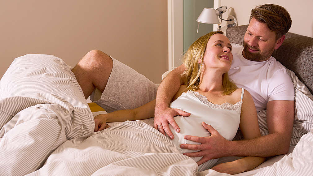 Schwangere Frau und Partner liegen auf dem Bett