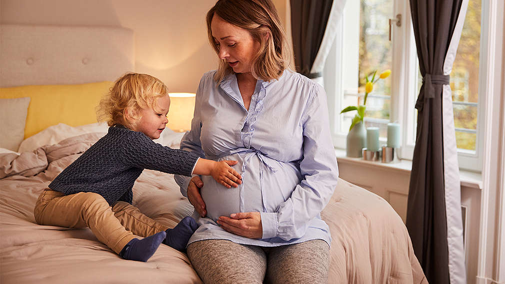 Schwangere sitzt mit Sohn auf dem Bett