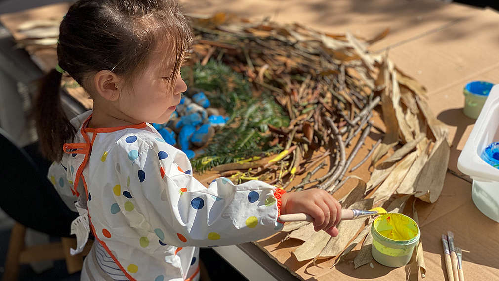 Kind bastelt einen Regenbogen aus Blätter, Ästen und Steinen