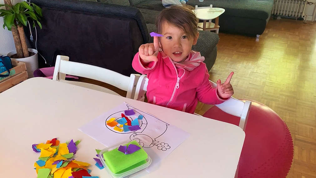 Kind bastelt ein Schnipselbild mit Schneckenmotiv