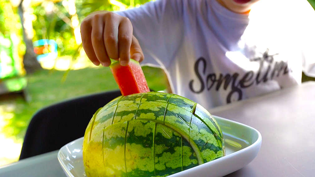 Kind greift nach einem zugeschnittenen Melonenstück