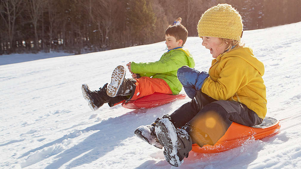 Zwei Kinder rodeln den Berg hinunter