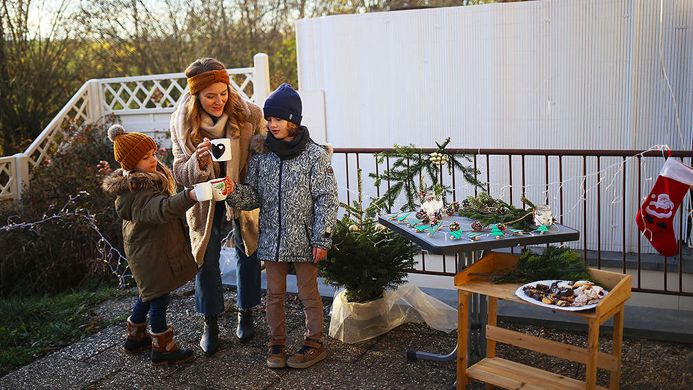 Mutter mit zwei Kinder trinkt einen Weihnachtspunsch auf einem geschmückten Balkon