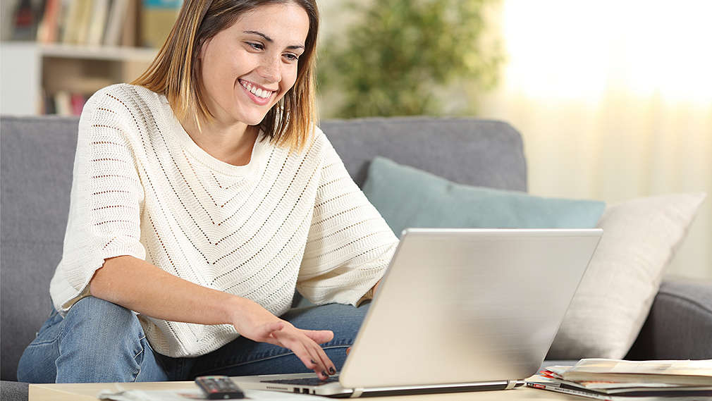 Frau sitzt auf der Couch und schaut in den Laptop