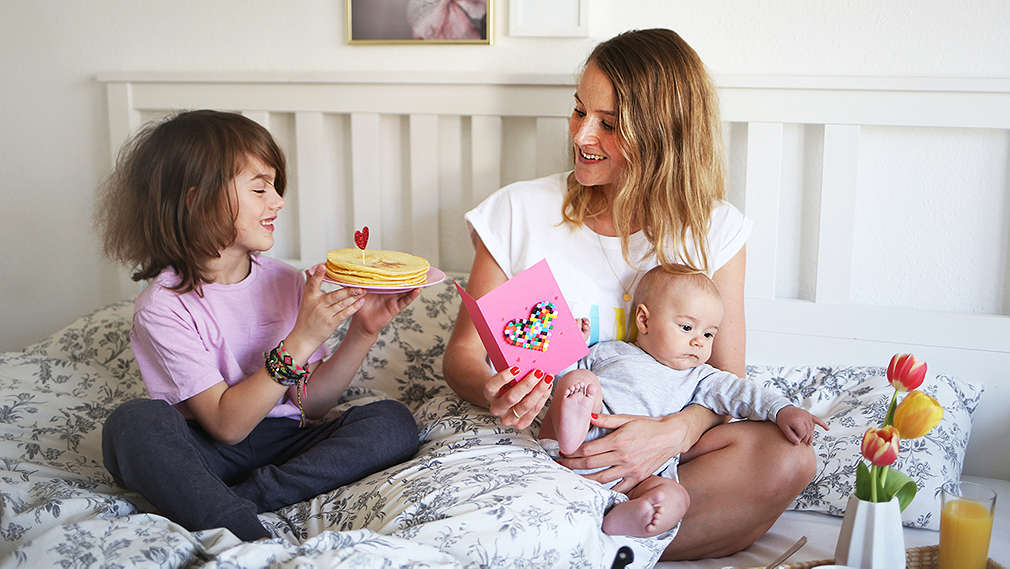 Mutter sitzt mit Kindern auf dem Bett