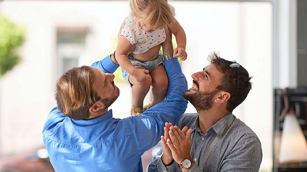 Zwei Väter lachen ihrem Kind zu