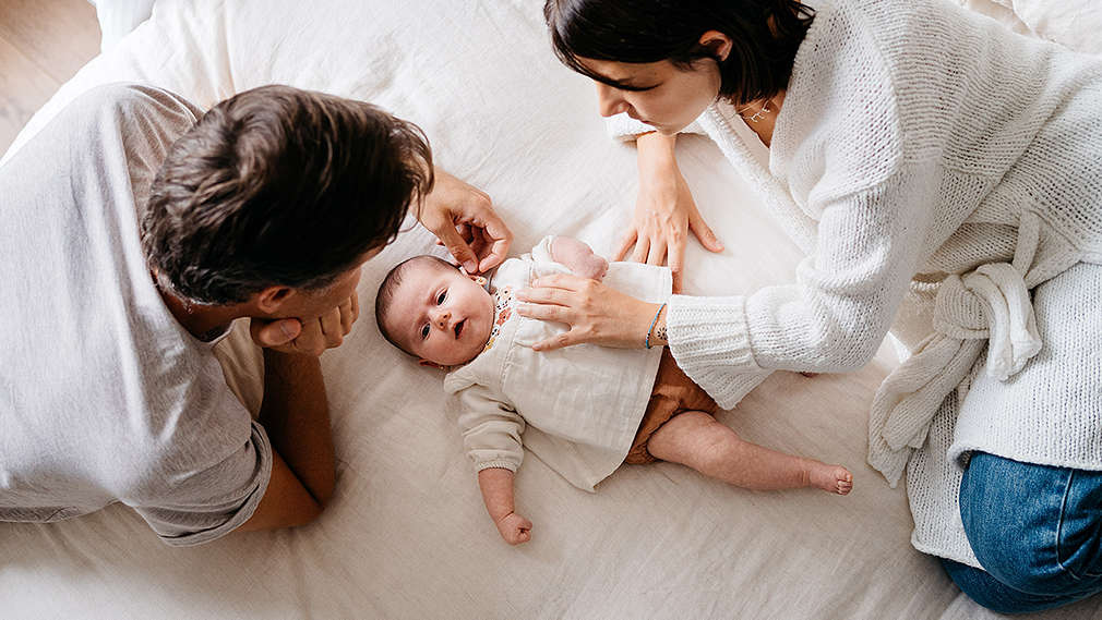 Eltern liegen mit Baby auf dem Bett