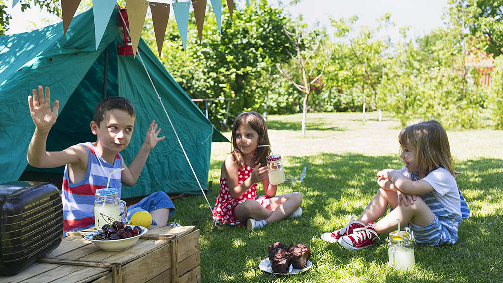 Drei Kinder sitzen vor einem Zelt