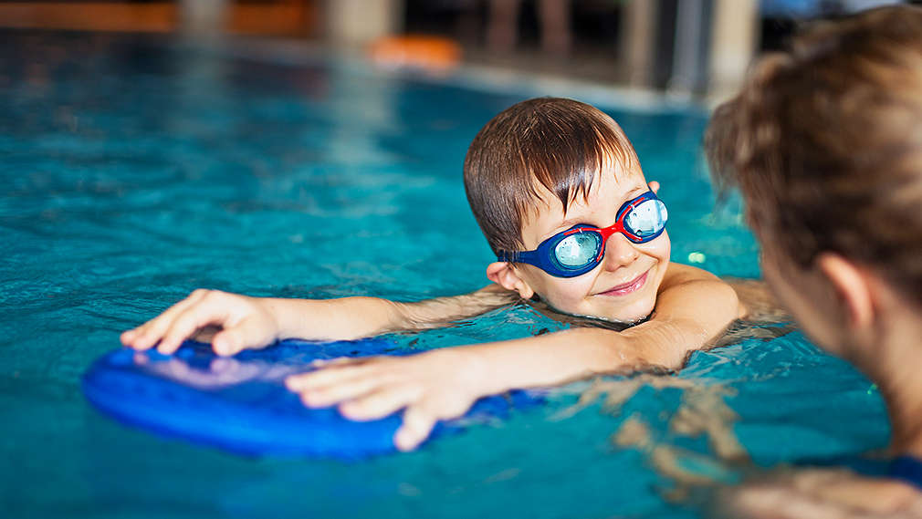 Frau hilft Jungen beim Schwimmen mit Schwimmbrett