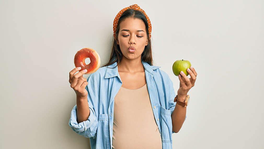 Eine Frau hält in der einen Hand einen Apfel und in der anderen einen Donut