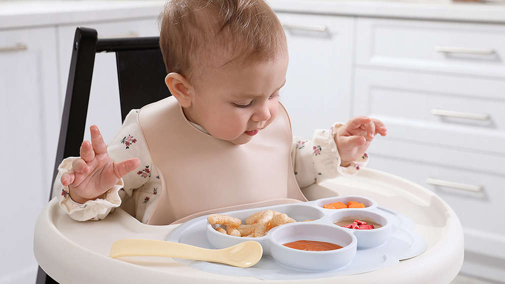 Baby sitzt im Hochstuhl und betrachtet seine Mahlzeit