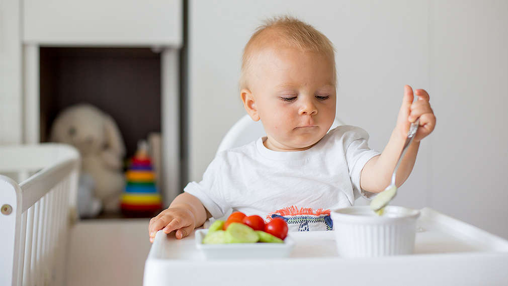 Baby sitzt im Hochstuhl vor seiner Mahlzeit