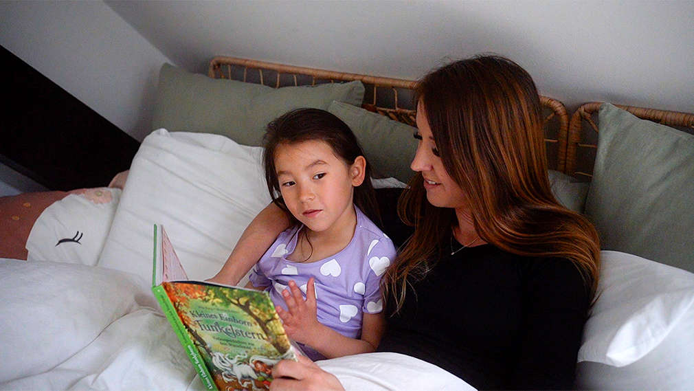 Mutter und Tochter lesen im Bett gemeinsam ein Buch vor dem Schlafengehen