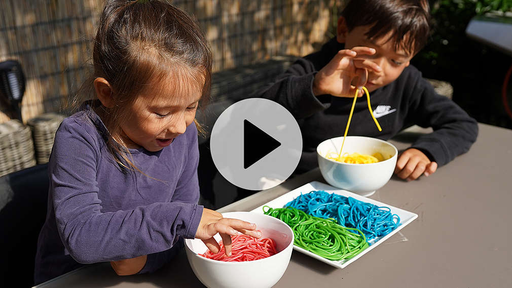 Zwei Kinder essen bunte Nudeln