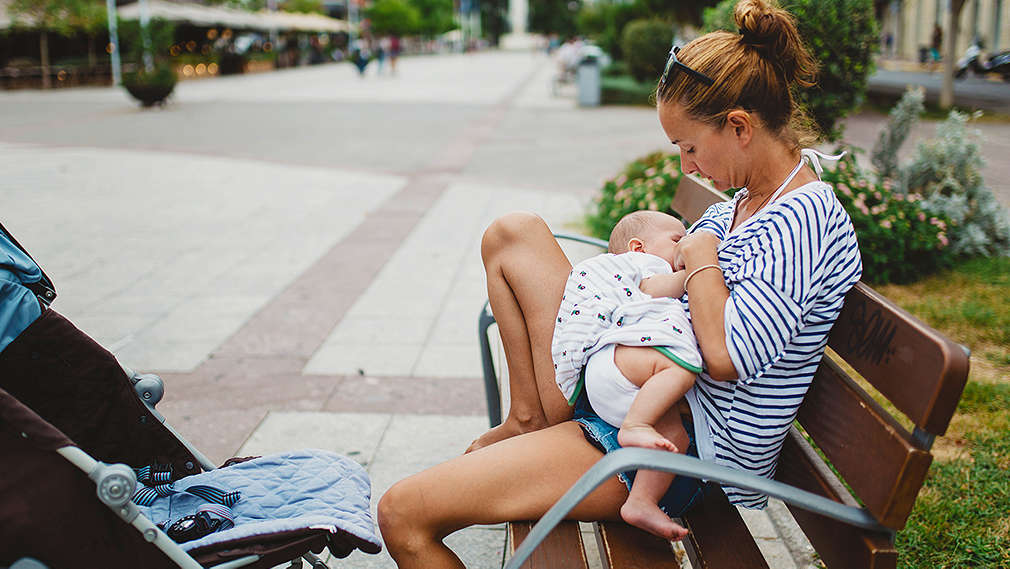 Frau stillt Baby auf einer Parkbank