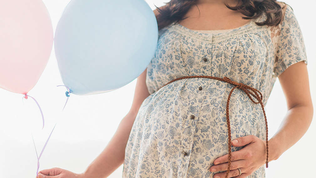 Schwangere Frau mit einem rosanen und einem blauen Luftballon