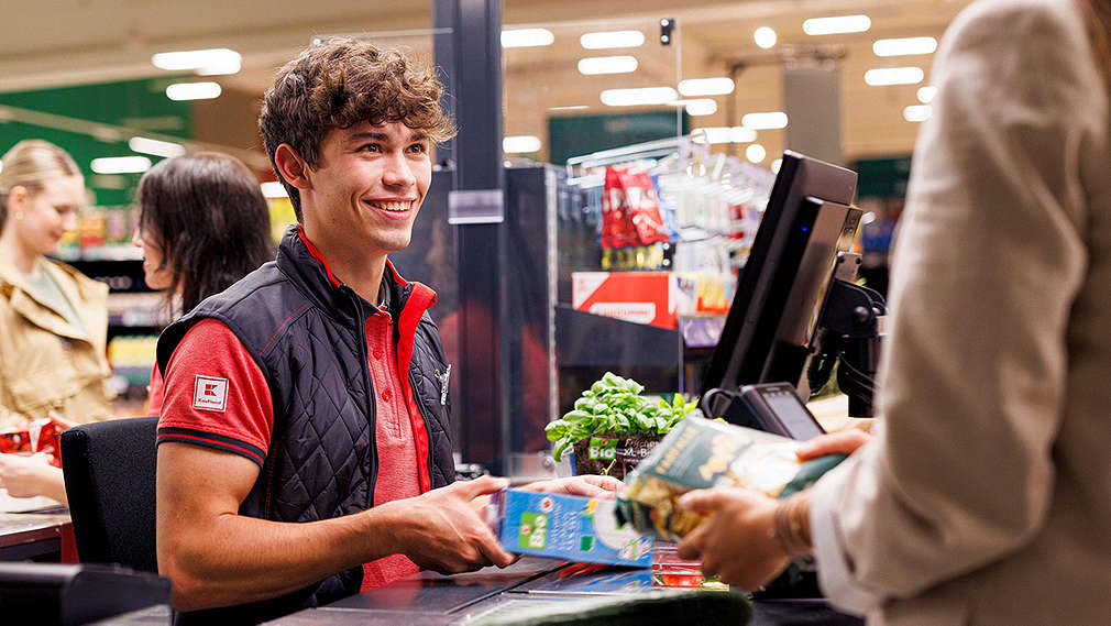 Filialmitarbeiter sitzt an der Kasse und kassiert Milch.