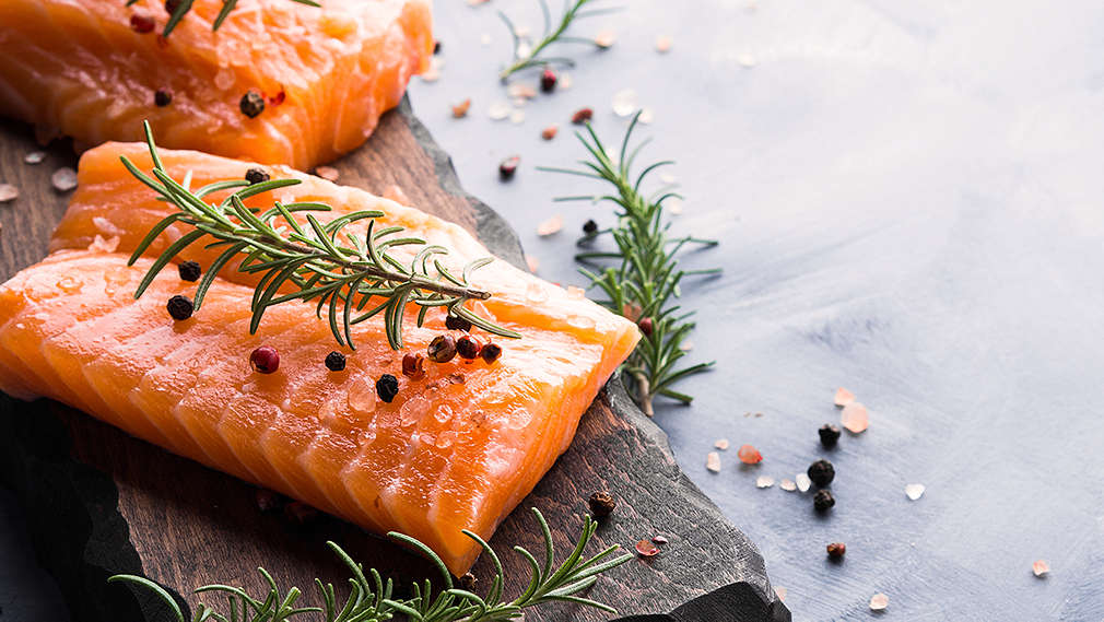 Frischer Lachs auf Holzbrett, dekoriert mit frischen Gewürzen wie Salz und Pfeffer.