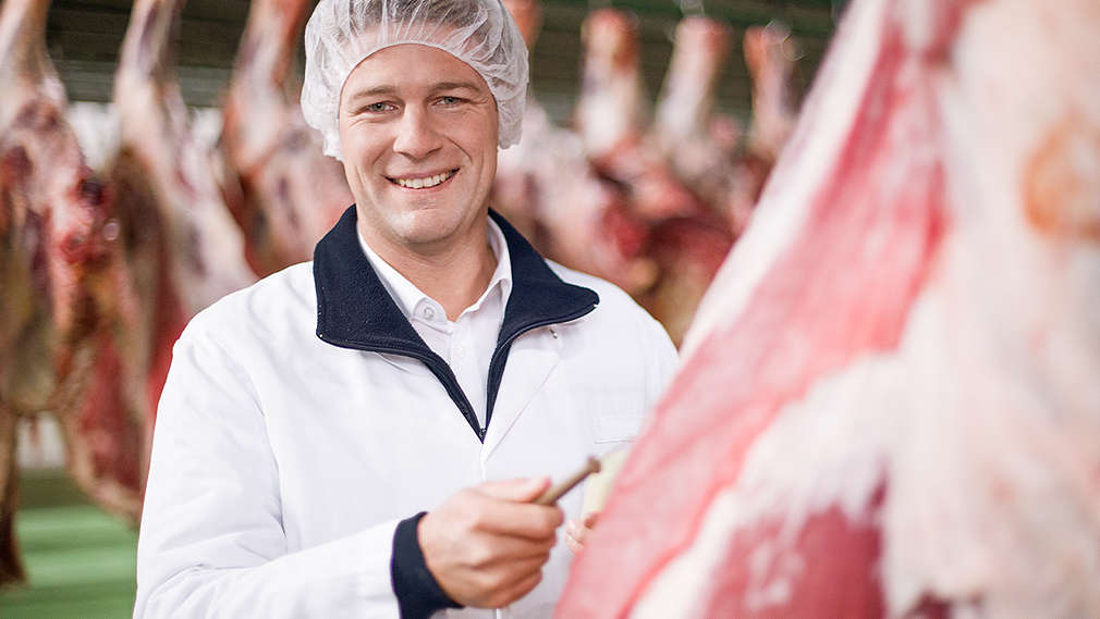 Metzger steht in Fleischwerk zwischen Teilstücken vom Schwein und Rin