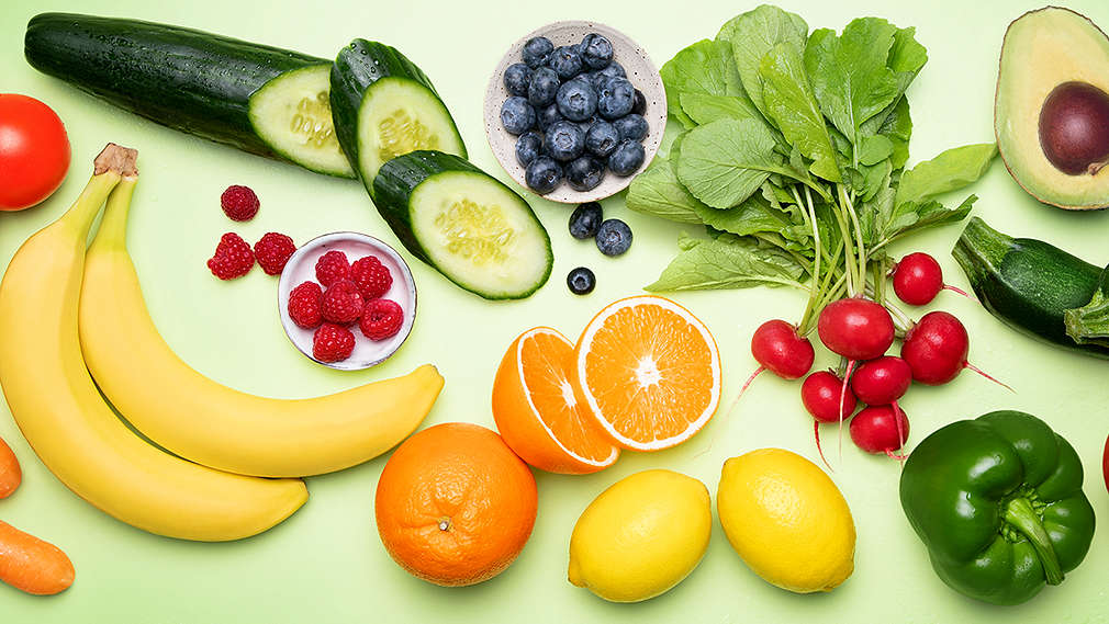 Verschiedene Obst- und Gemüsesorten teilweise aufgeschnitten auf hellgrünem Hintergrund.