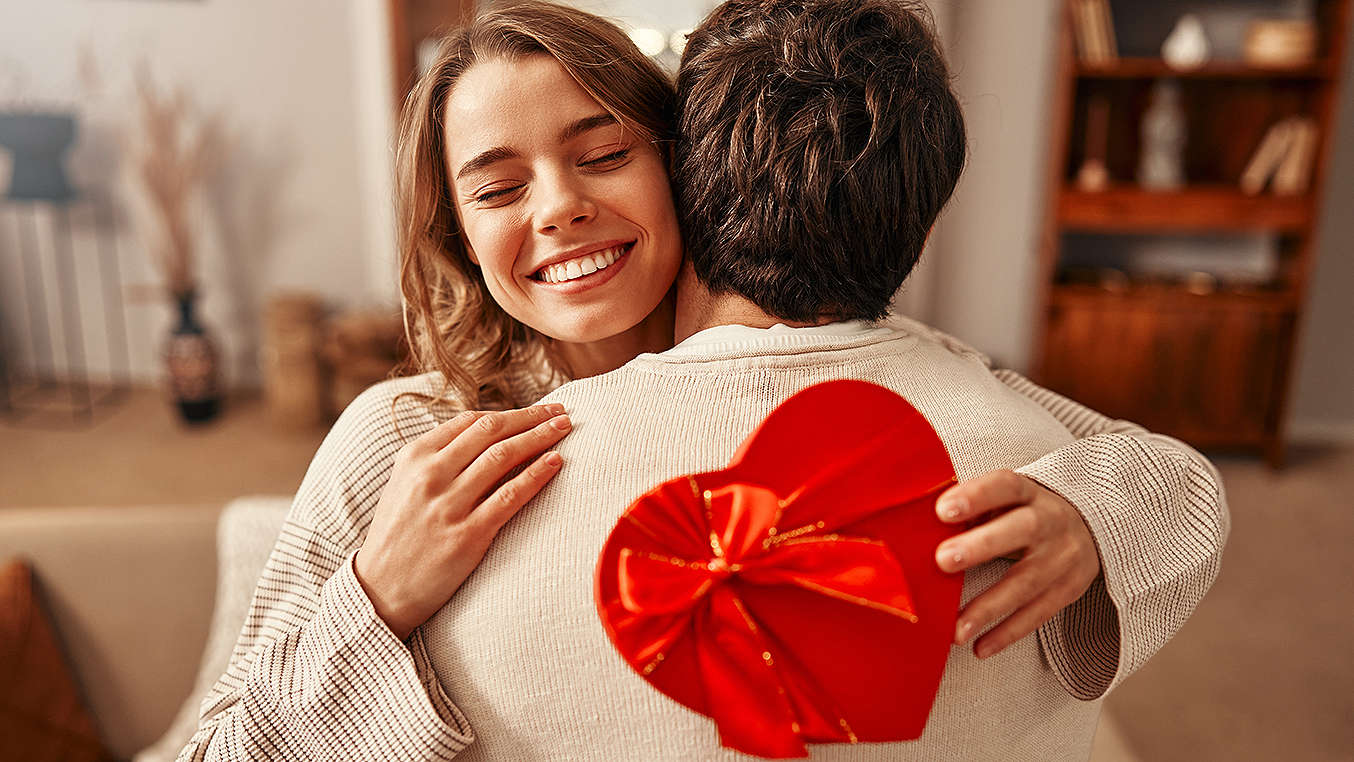 Zwei Personen umarmen sich; Frau hält eine Herz-Schachtel in der Hand