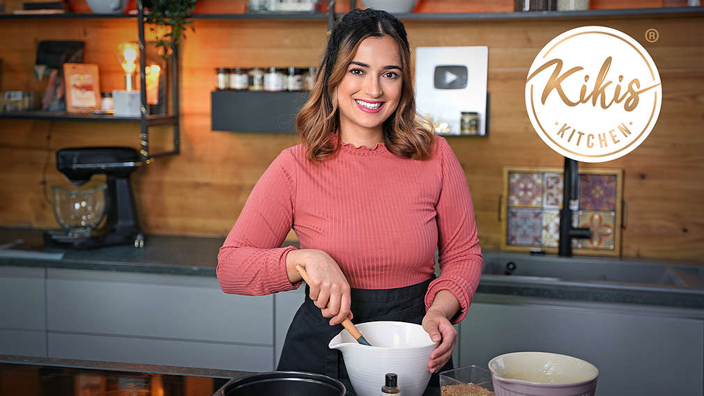 Kiki von Kikis Kitchen rührt einen Teig in einer Rührschüssel an; Logo: Kikis Kitchen