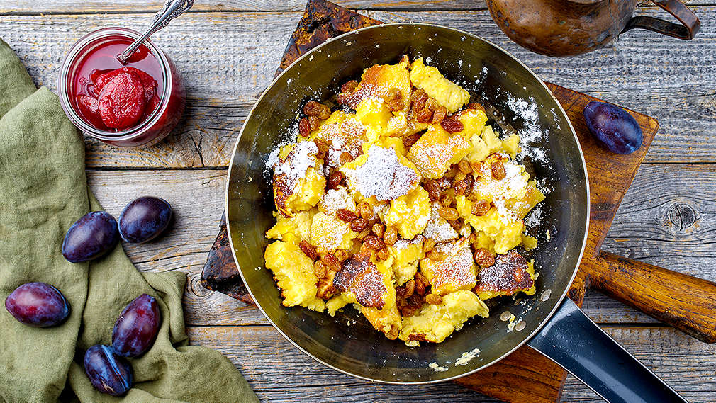 Mehrere Personen in Tracht sitzen an einem mit Alpengerichten bedeckten Tisch