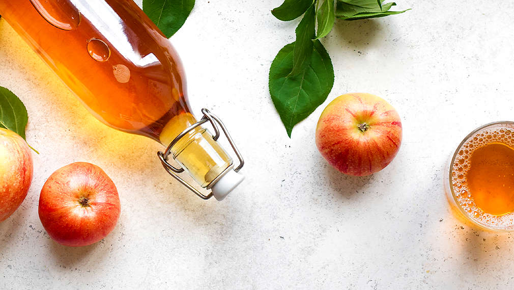 Eine Flasche mit Apfelessig, Äpfel und ein Glas mit Apfelessig
