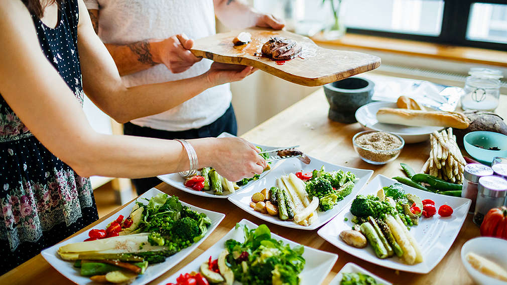 Zwei Personen verteilen Fleisch auf verschiedene Teller mit Gemüse