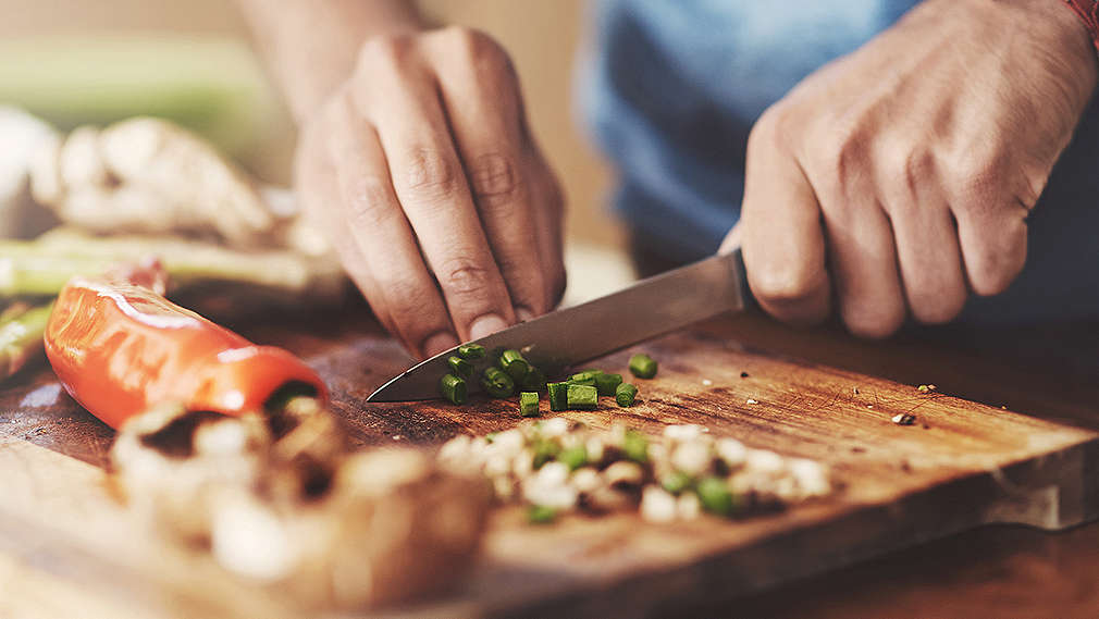 Koch schneidet Gemüse mit einem Küchenmesser auf einem Holzschneidebrett 