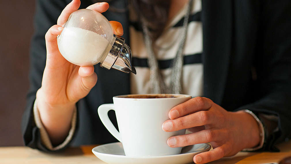 Person streut Zucker in den Kaffee