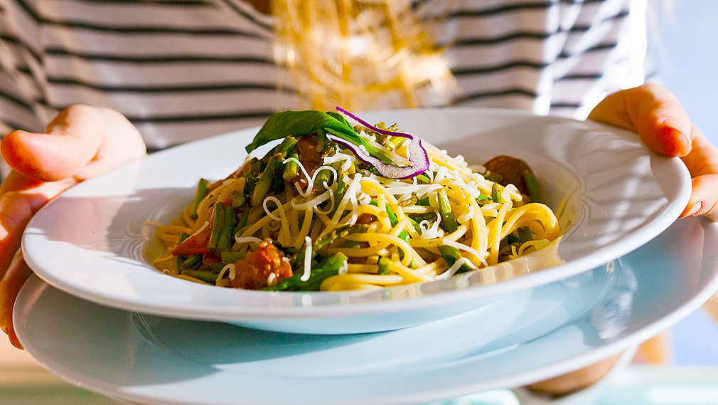 Frau hält einen Teller Spaghetti mit Gemüse in den Händen