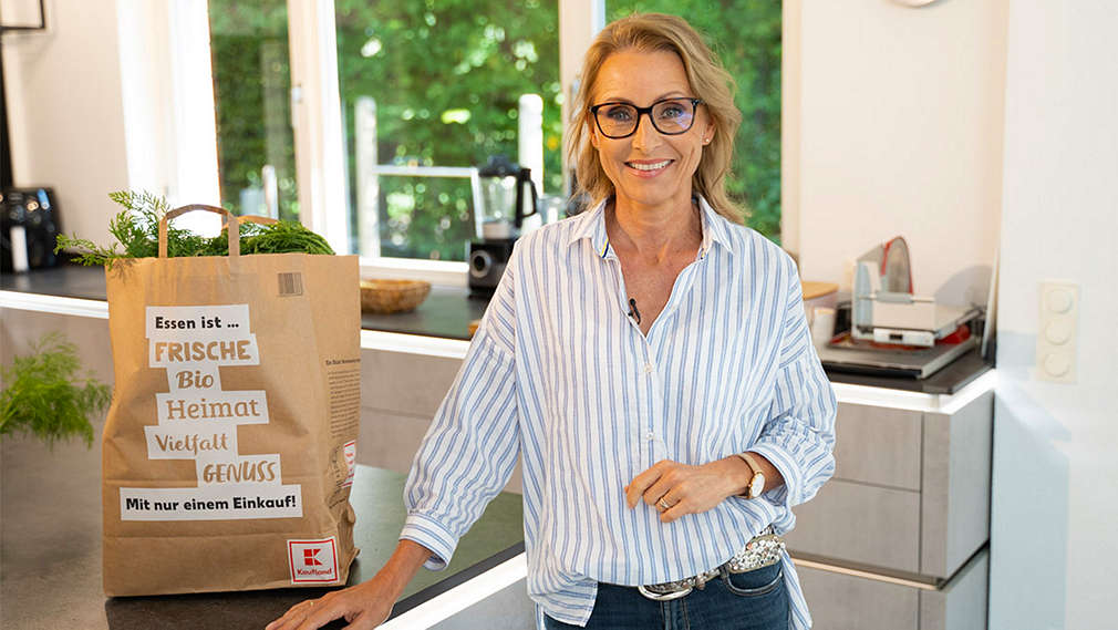 Dr. Alexa Iwan steht an Küchenzeile, darauf steht eine Kaufland-Papiertasche