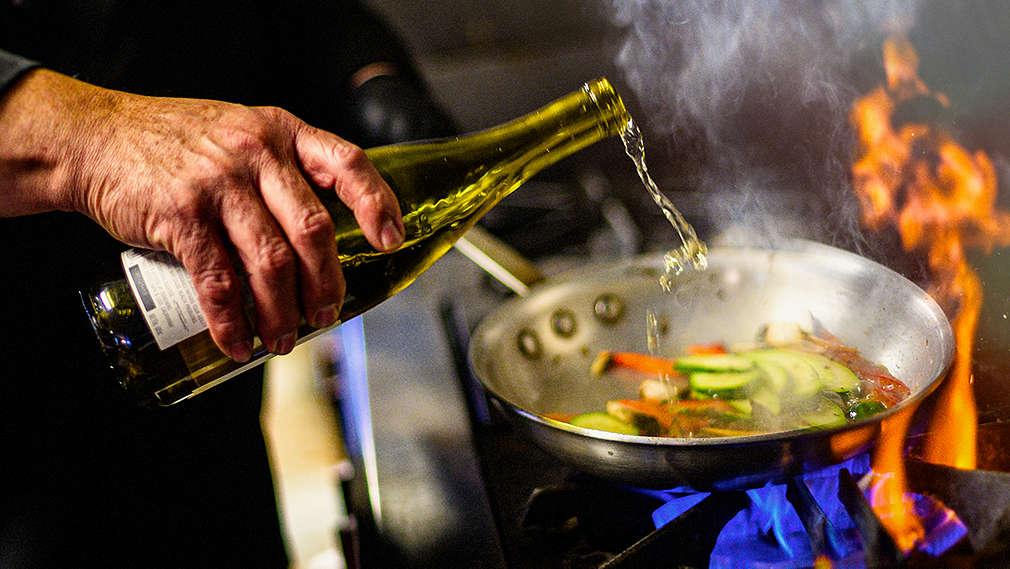 Koch löscht mit Wein das gebratene Gemüse in einer Bratpfanne ab