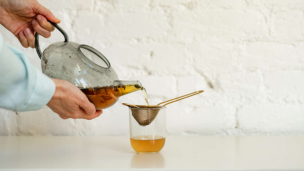 Aufgebrühter Tee wird durch ein Sieb in eine Tasse gegossen