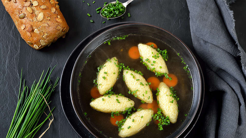 Suppe mit abgestochenen Nocken in einem schwarzen Teller, verfeinert mit Schnittlauch.