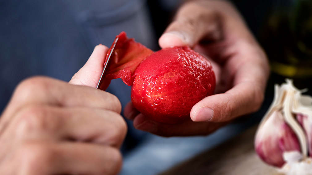 Die Haut einer Tomate wird im Close-up abgezogen.