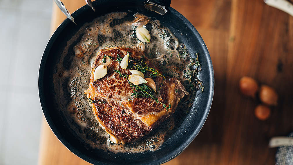 Steak wird mit frischen Kräutern und Knoblauch in einer Pfanne angebraten