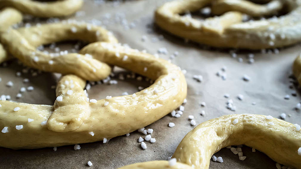 Brezel mit Salz bestreut werden auf einem Backblech mit Backpapier aufgebacken