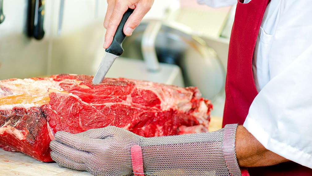 Mit einem Messer werden aus einem großen Stück Fleisch die Knochen entfernt