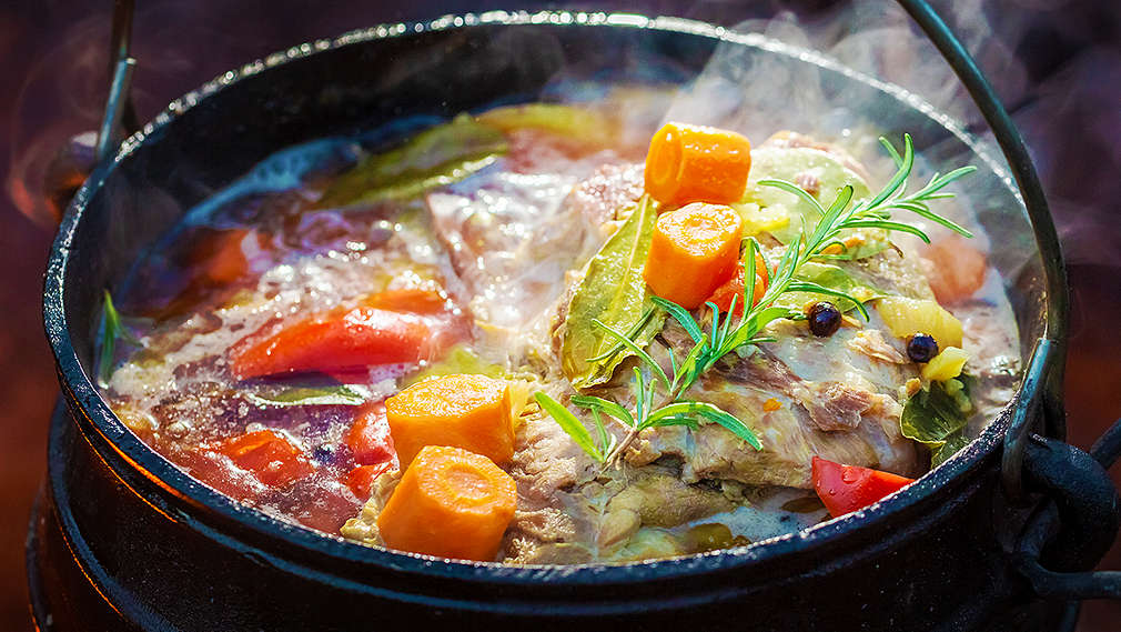 Ein seitlich von oben fotografierter Feuertopf mit viel Gemüse über offener Flamme
