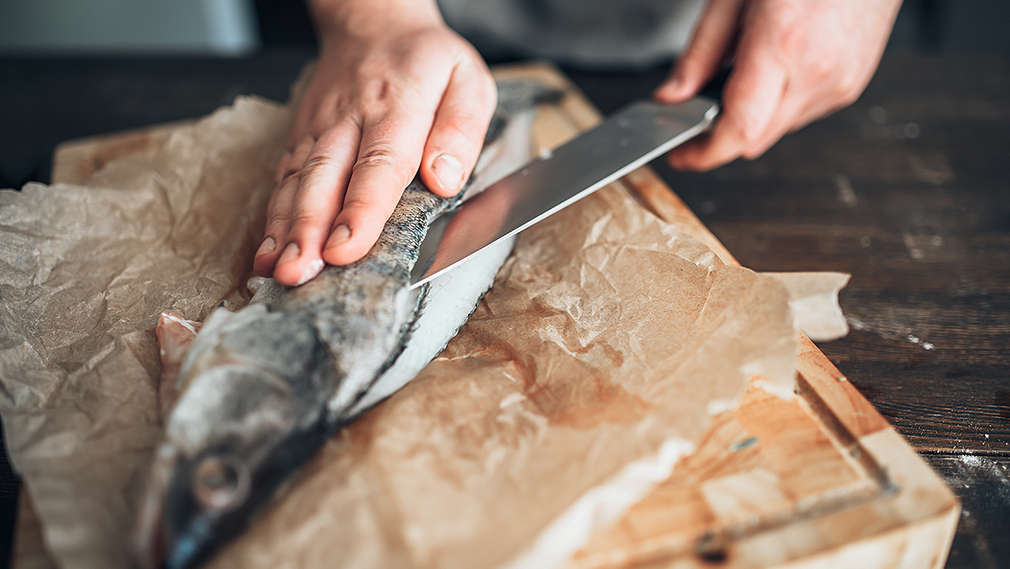 Eine Forelle wird mit einem Küchenmesser auf einem Holzbrett filetiert