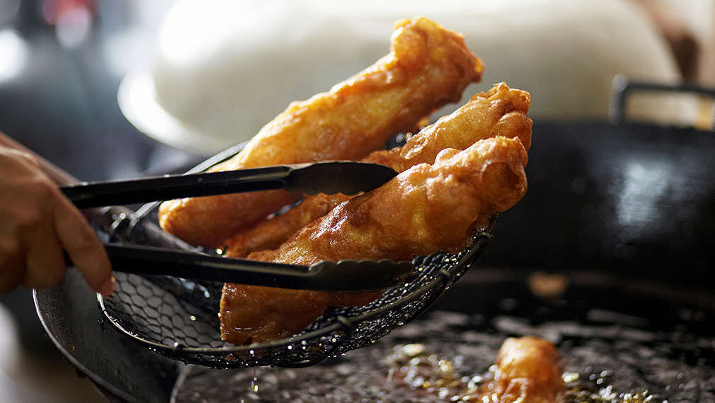 Frittiertes Gemüse wird mit einer Schöpfkelle und Zange aus der Pfanne genommen