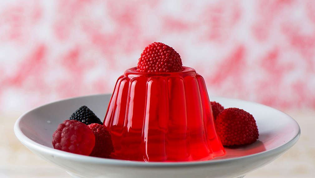 Rotes Gelee oder Wackelpudding steht in einem Teller und mit Obst dekoriert auf einem Küchentisch