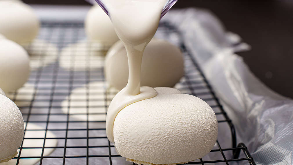 Eine Süßspeise liegt auf einem Gitter und wird mit weißer Glasur überzogen.