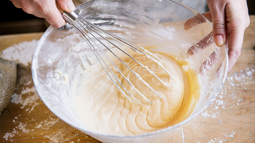 Eine Glasschale, in der Teig mit einem Schneebesen glatt gerührt wird.