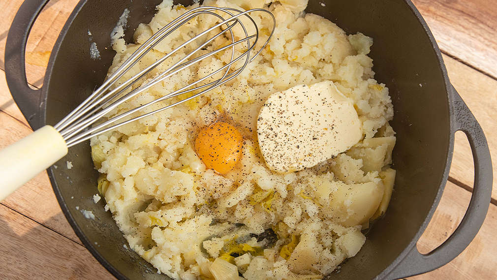 Ein Eigelb, Butter und Gewürze werden in Kartoffelbrei gerührt