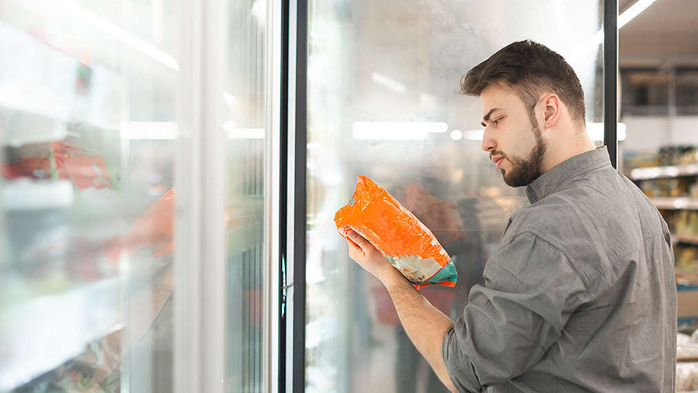 Kunde steht vor einem Kühlregal und liest das Mindesthaltbarkeitsdatum von einer Produktverpackung ab