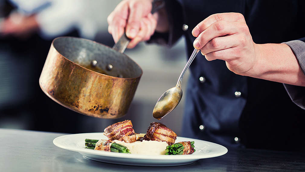 Person gießt Soße über ein fertig zubereitetes Gericht