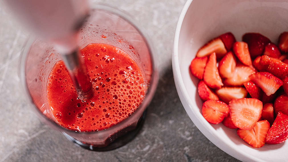 Kleingeschnittene Erdbeeren werden in einer Schale mit einem Handmixer püriert